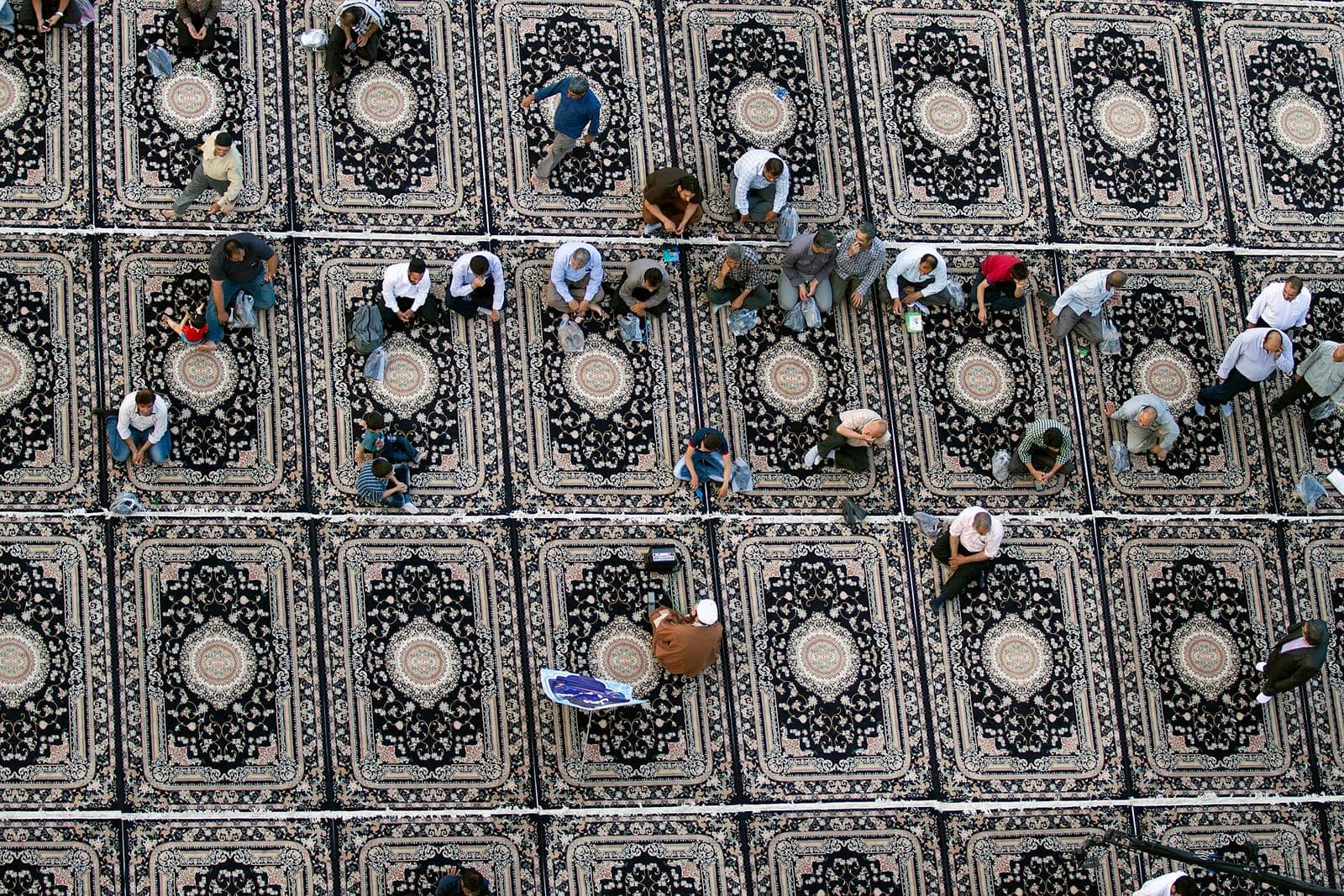 نمای بالا از جمع حاضران نشسته بر فرشهای نقشدار شبستان مسجد