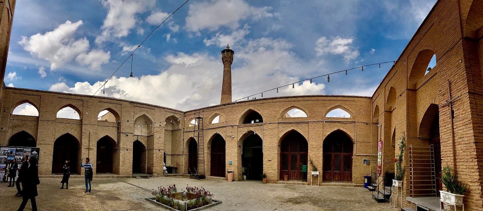صحن مسجد جامع سمنان با رواقهای آجری دوطبقه و منارهٔ تاریخی در پسزمینه